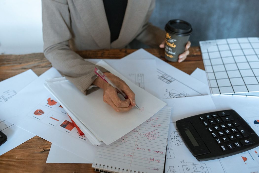 A person making notes while reviewing printed documents at a desk